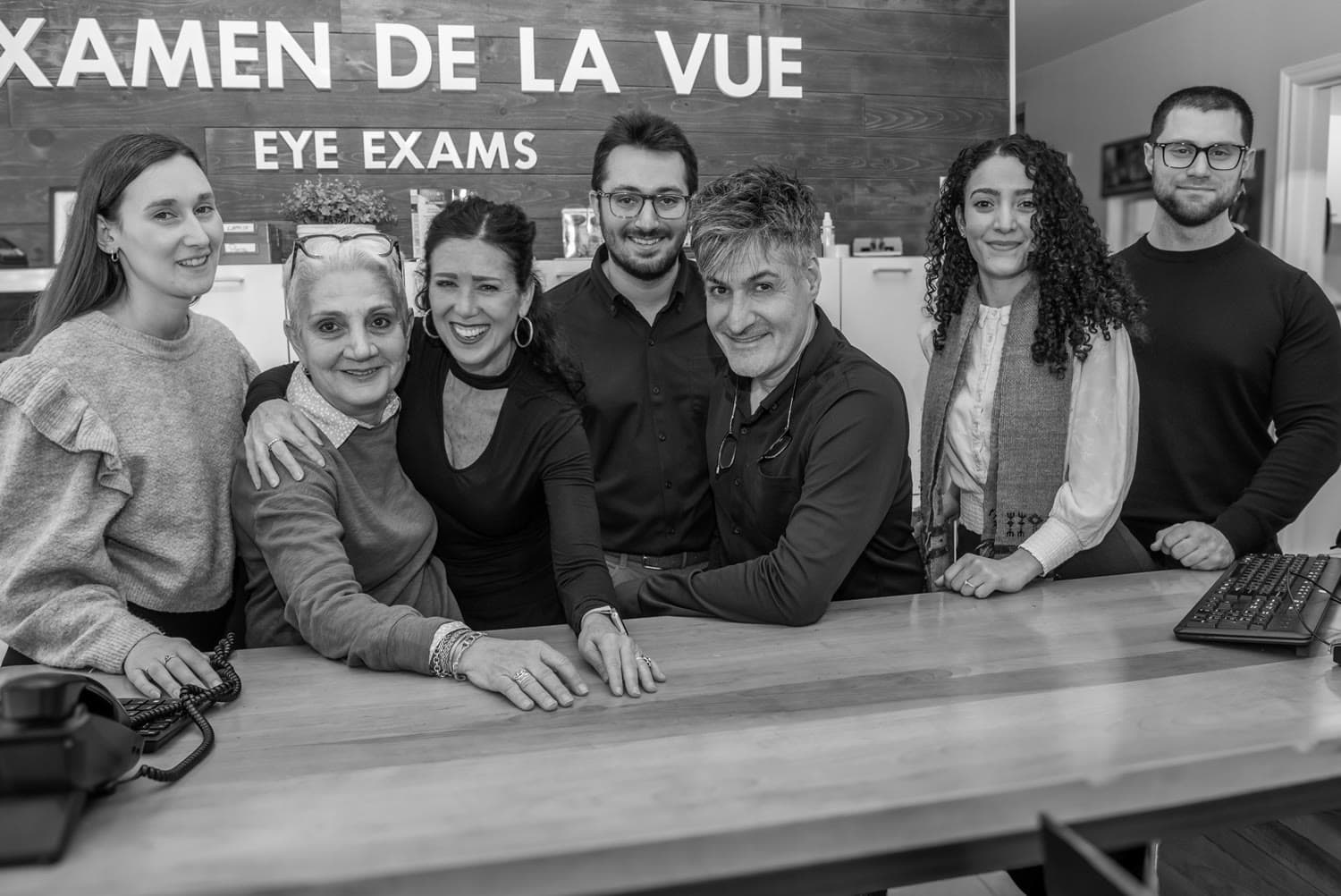L'équipe de la boutique Saint-Laurent réunie au comptoir, sous les lettres de bois « Examen de la vue / Eye exams ».